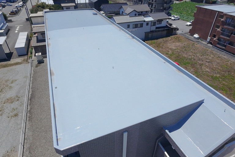 <p>施工後は、屋上全体に継ぎ目のないウレタン塗膜防水層が形成され、美観だけでなく高い防水性能を備えた屋上へと生まれ変わりました。<br>

通気緩衝工法を採用することで、防水層内部に発生する湿気を脱気筒から効率よく排出し、防水層の膨れを抑制。長期間にわたり安定した防水性能を維持できる仕様となっています。<br>

また、改修用鉛ドレンや塩ビ配管の交換、外壁タイルへの浸透性吸水防止剤施工まで実施したことで、雨漏り対策だけでなく建物全体の耐久性・安全性も向上しました。<br>

使用材料・施工内容<br>

屋上防水改修工事<br>

・既存ゴムシート防水撤去<br>
・既存浮き部塗膜防水撤去<br>
・高圧洗浄<br>
・防水下地処理<br>
・ウレタン塗膜防水 通気緩衝工法（PN-V20G）<br>
・ウレタン塗膜防水 メッシュ工法（PGT-V20G）<br>
・脱気筒取付<br>
・改修用鉛ドレン設置<br>
・立上り防水施工<br>

構造物補修工事<br>

・タイル外壁高圧洗浄<br>
・打診調査・目視調査<br>
・コンクリート構造物補修<br>
・浸透性吸水防止剤 タイルセラクリーン施工<br>

設備工事<br>

・塩ビ配管取替工事<br>
・ジョイント交換<br>
・エルボ交換<br>
・金物交換<br>

仮設工事<br>

・仮設足場工事<br>
・昇降設備設置<br>
・安全対策<br>
・荷揚げ<br>
・廃材処分<br>

建物診断<br>

・ドローン無料建物診断<br>
・横井豊文教師建物診断調査</p><p><br></p>
