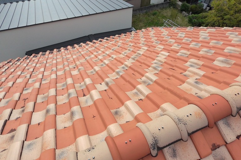 <p>岐阜県中津川市にて、戸建て住宅のドローンを活用した無料建物診断を実施いたしました。<br>

今回は、地上からでは状態を確認しにくい屋根を中心にドローンで撮影し、屋根材全体の状態や棟部分などを確認しました。<br>

屋根にはオレンジ系とホワイト系を組み合わせた洋瓦が使用されています。調査では、瓦表面の広い範囲に黒ずみや汚れの付着、経年による変色が確認できました。特に瓦の重なり部分や水が流れる箇所では黒ずみが目立っており、長年の雨風や湿気などの影響を受けている状態がうかがえます。<br>

また、棟部分や屋根全体の並びについてもドローン画像で確認しました。現時点の写真では大きく瓦がずれている箇所は目立ちませんが、瓦屋根は地上から細かな状態を把握することが難しいため、定期的に上空から状態を確認しておくことが大切です。<br>

株式会社横井では、ドローン無料調査と横井豊史教師建物診断により、屋根材だけでなく建物全体の状態を確認しています。</p><p><br></p>
