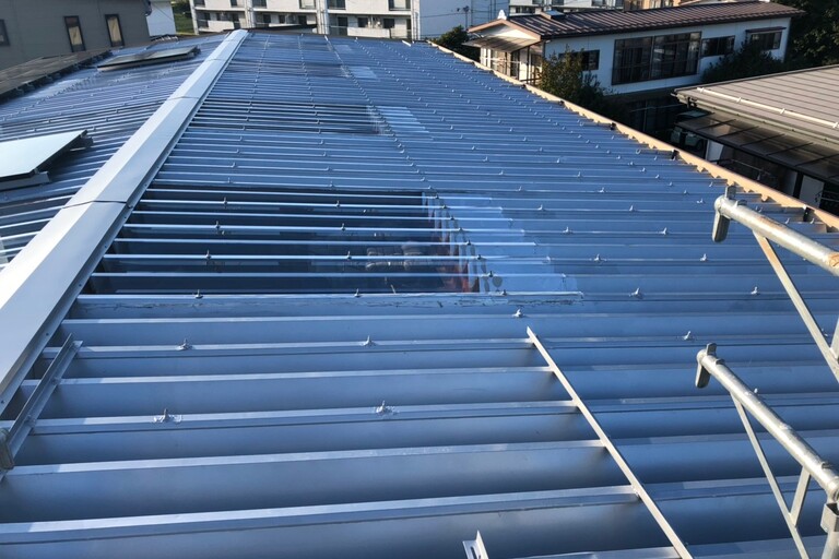 <p>施工では、屋根上の太陽光パネル24枚を一時取り外し、施工後に復旧・ケーブルの緊結直しを行いました。<br>

鉄板屋根約226.8㎡は高圧洗浄で汚れや付着物を除去し、下塗りに「2液サビカット」、中塗り・上塗りに「ユメロックルーフ」を使用。防錆性・耐候性を高め、屋根全体を保護しました。<br>

ポリカ折板部分は既存32枚を撤去し、耐候グレード・厚さ2.0mmの「ポリカ折板Y500」32枚へ交換。新規ボルト施工や既存波板の廃棄処分まで一貫して行いました。<br>

使用材料・施工内容<br>

＊鉄板屋根塗装：約226.8㎡<br>
＊高圧洗浄：約226.8㎡<br>
＊下塗り：2液サビカット<br>
＊中塗り・上塗り：ユメロックルーフ<br>
＊ポリカ折板Y500：32枚／耐候グレード・t=2.0mm<br>
＊既存波板撤去・新規ボルト施工<br>
＊太陽光パネル24枚：一時取り外し・復旧</p><p><br></p>