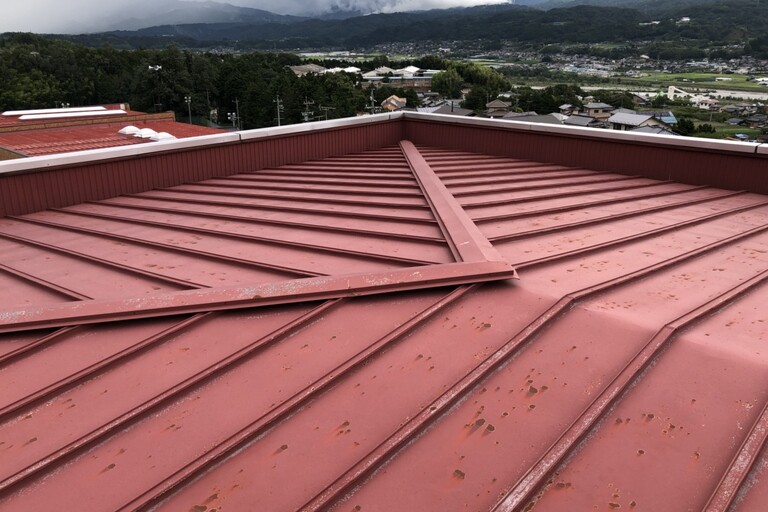 <p>長野県下伊那郡高森町の「高森町役場庁舎」にて、屋根の塗装・防水工事をご依頼いただきました。<br>

庁舎屋根は常に紫外線や雨風の影響を受けるため、経年による塗膜の劣化や防水性能の低下が進みやすい部分です。現地調査では、東棟・北南棟の屋根や樋、立上り部分などを確認し、既存塗膜の状態に合わせた下地調整と塗り替えが必要と判断しました。<br>

今回は高圧洗浄とRB種下地調整を行い、2液エポキシ系錆止め塗料で下塗り後、「ルーフスターSi」を2回塗布する仕様をご提案しました。<br>

＊ドローン無料調査<br>
＊横井豊史教師建物診断</p><p><br></p>